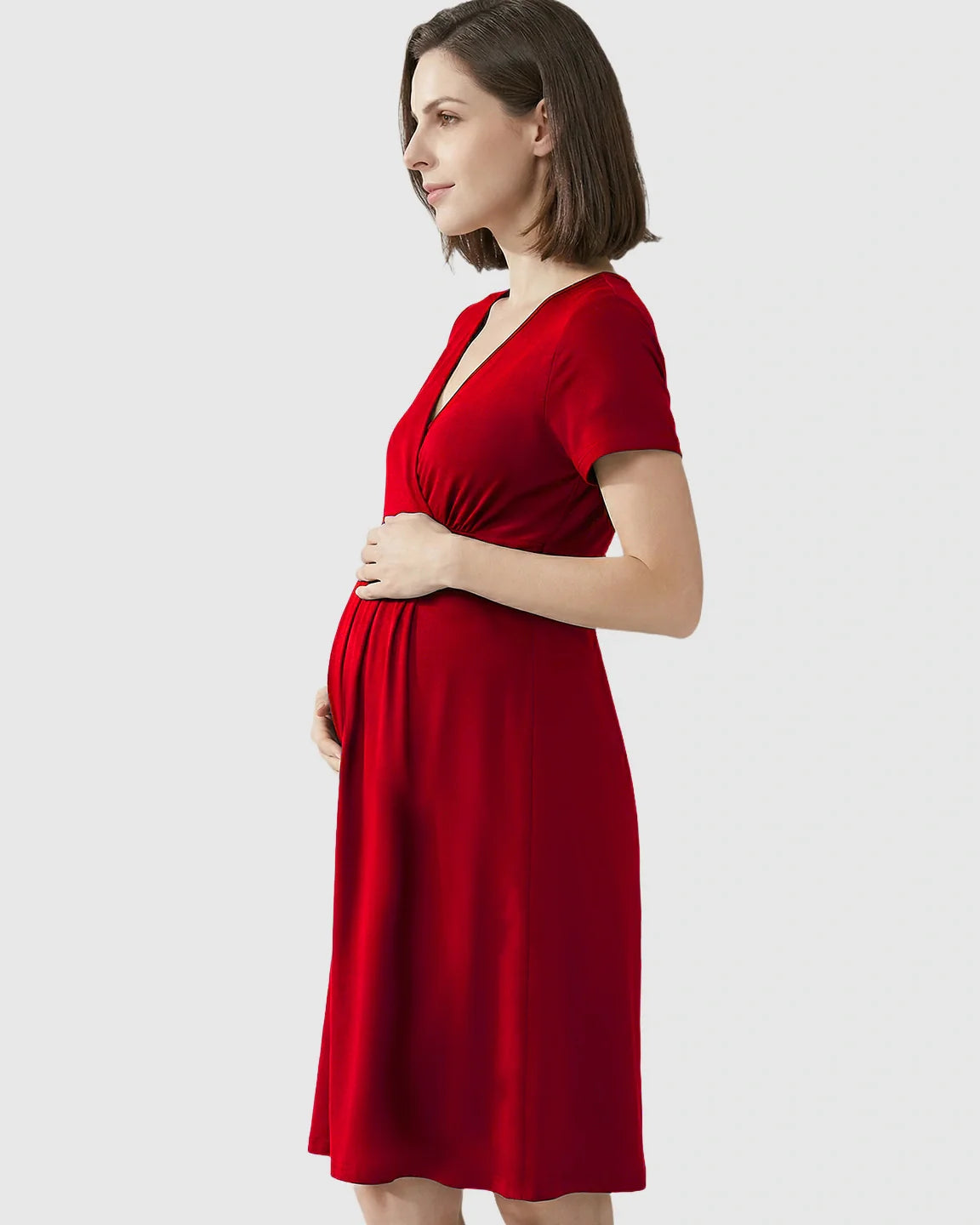Pregnant woman in a red V-neck A-line maternity and nursing dress, holding her baby bump.