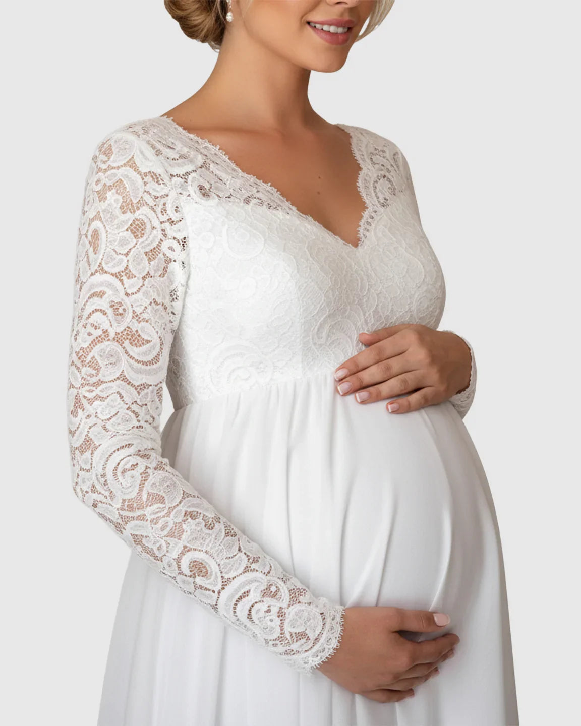 White lace maternity bridal gown with long sleeves, V-neck, and flowing skirt, worn by a smiling pregnant woman.