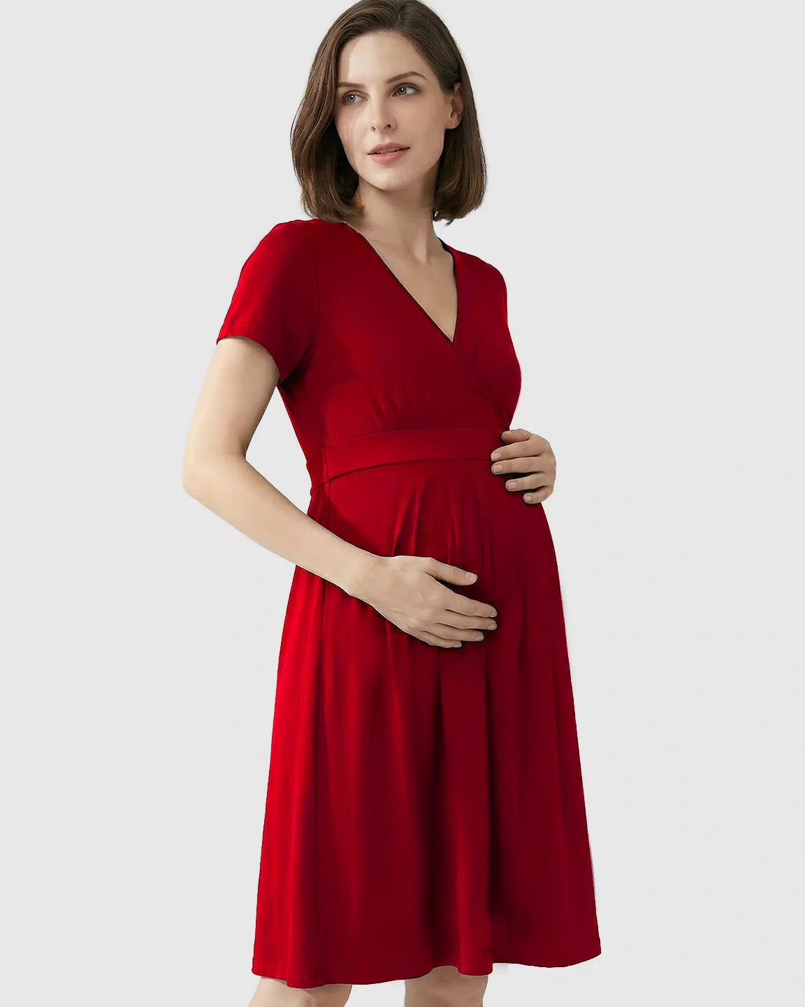 Pregnant woman in a red V-neck A-line maternity and nursing dress, holding her baby bump.