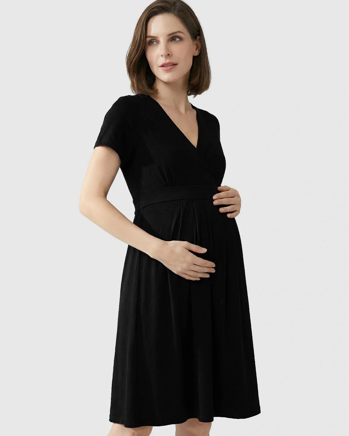 Woman wearing a black V-neck A-line maternity and nursing dress, hands on her baby bump.