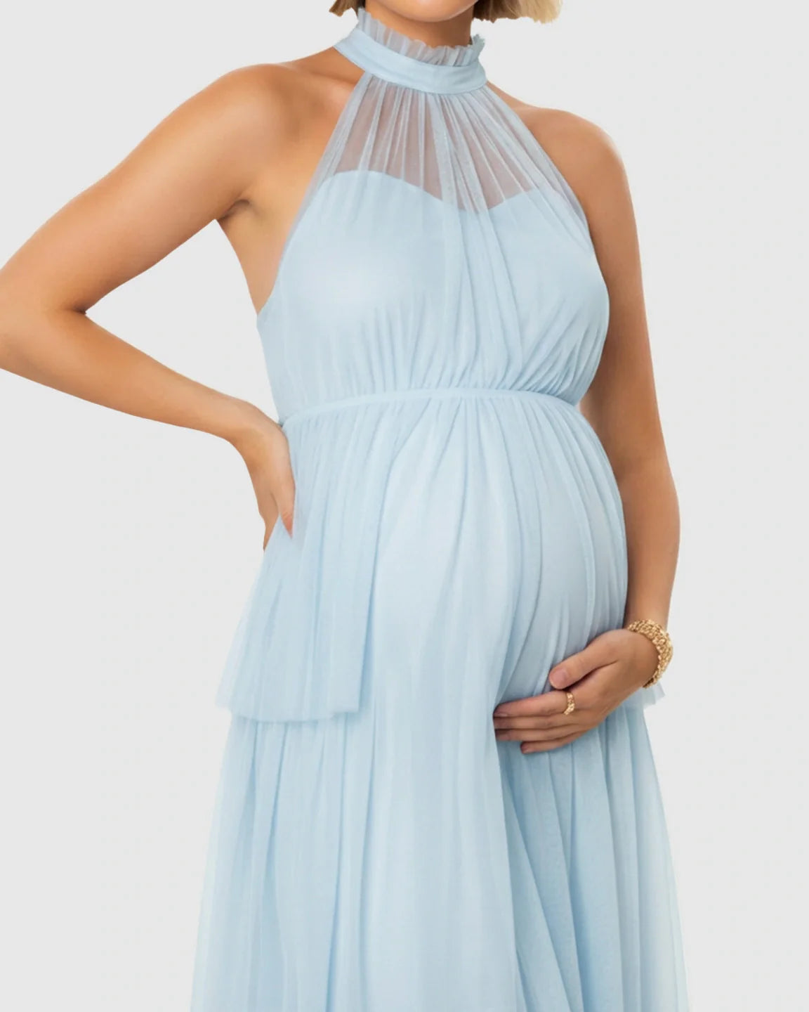 Pregnant woman in a light blue halter neck tiered mesh maternity gown, showcasing the bump.