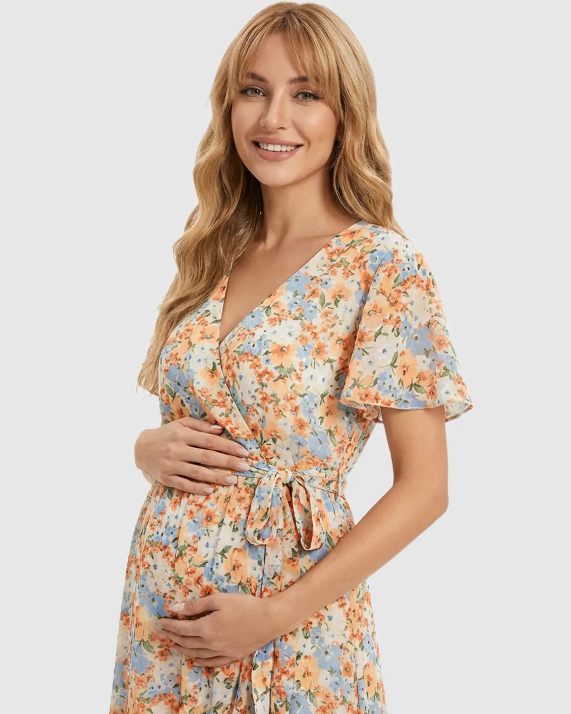 Smiling pregnant woman in a floral V-neck ruffled hem maternity midi dress with a tie waist.