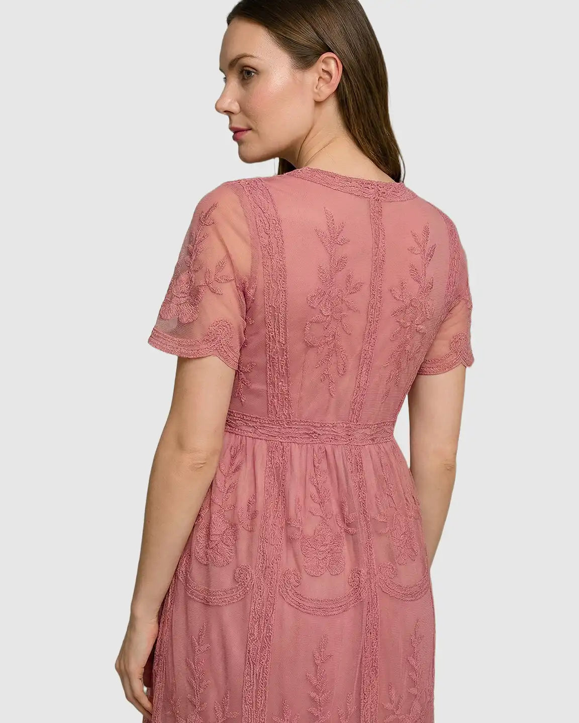 Woman in a pink lace maternity midi dress with V-neck, short sleeves, and floral embroidery.