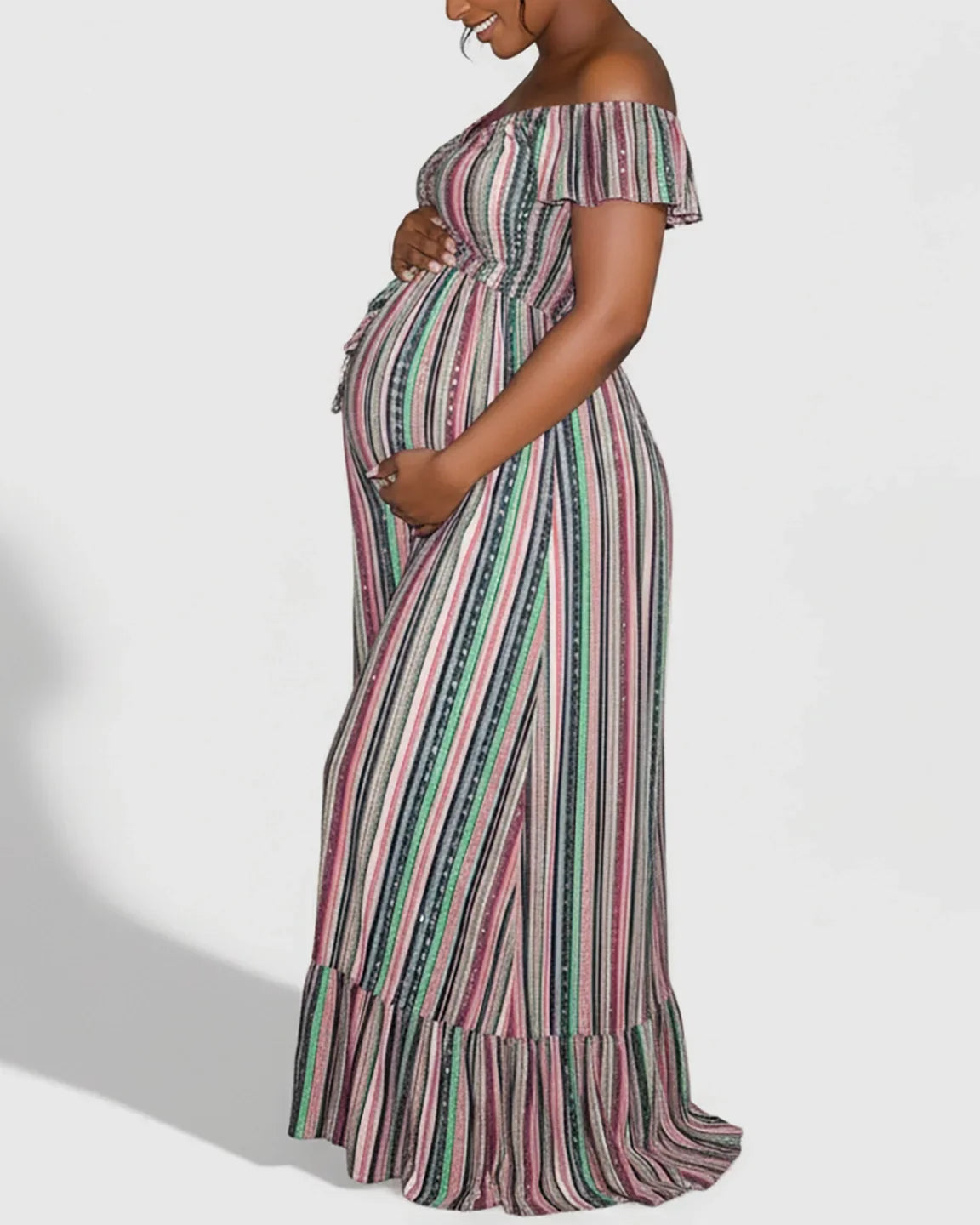 Pregnant woman in an off-shoulder, floor-length maternity maxi dress with colorful vertical stripes and a tie-up waist.