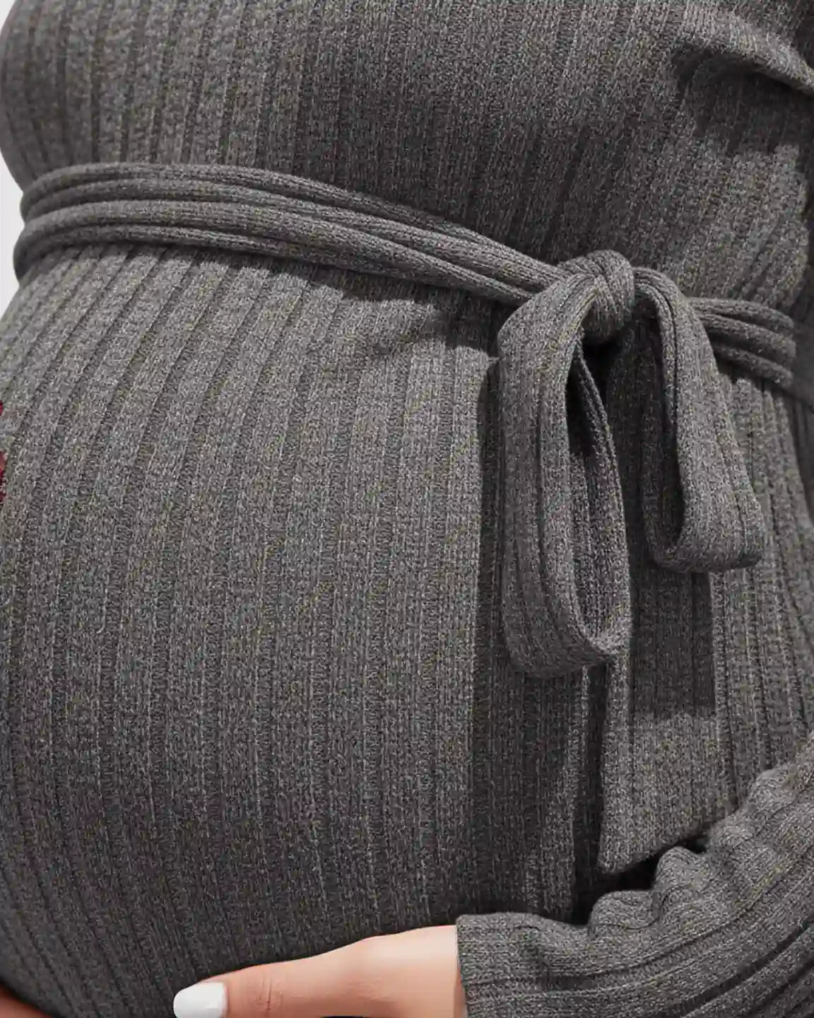 Close-up of a pregnant belly in a gray ribbed knit maternity sweater with a tied waist.