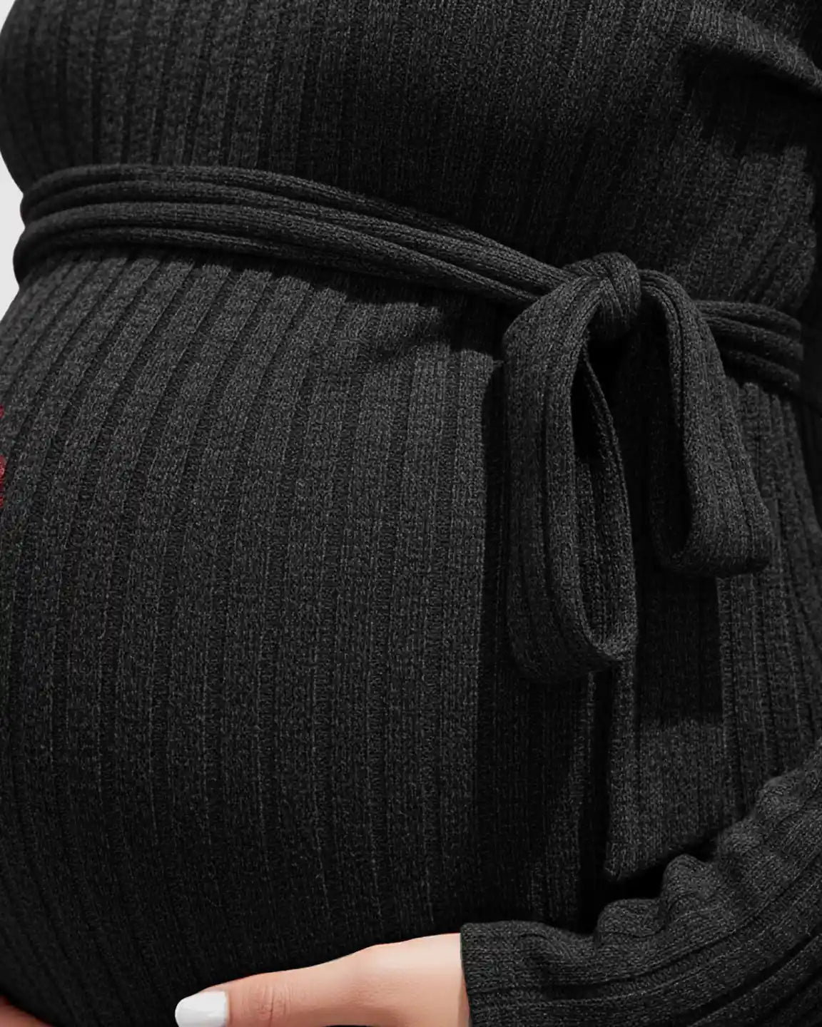 Close-up of a pregnant belly in a black ribbed tie-waist long sleeve maternity sweater.