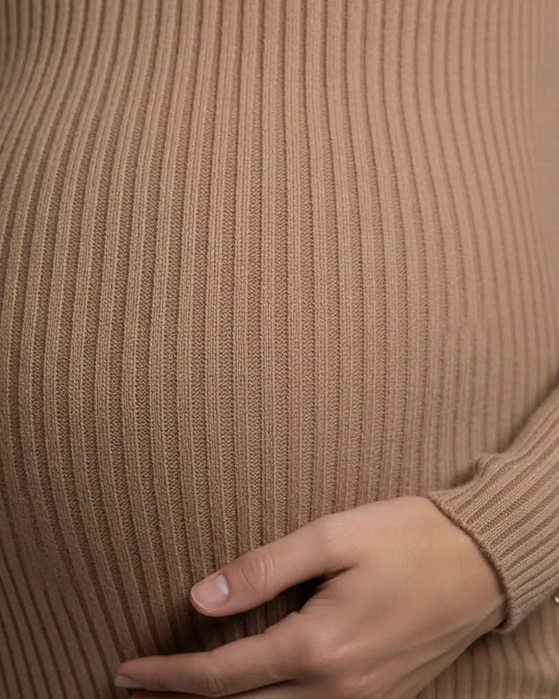 Pregnant belly in a beige ribbed knit bodycon maternity dress with a hand resting on it.