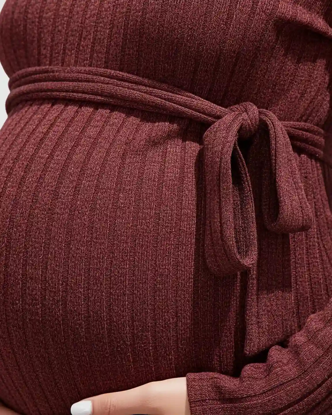 Close-up of a pregnant belly in a ribbed, burgundy maternity sweater with a tied waist.