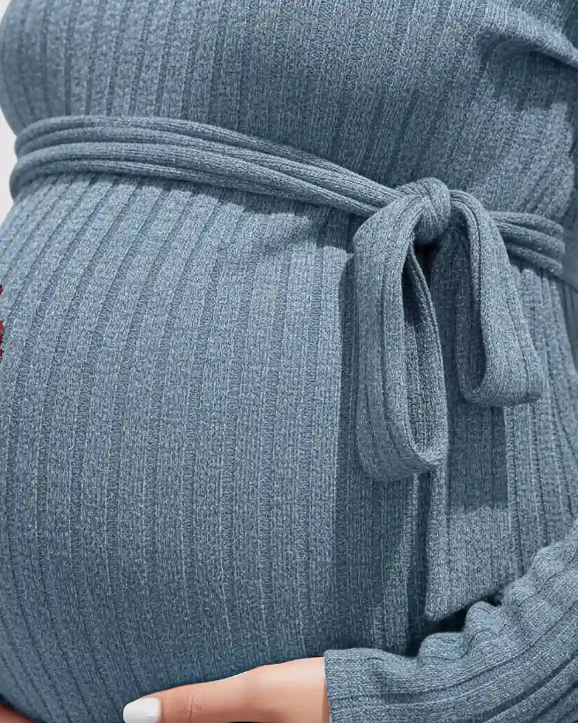 Close-up of a pregnant belly in a blue ribbed tie-waist long sleeve maternity sweater.