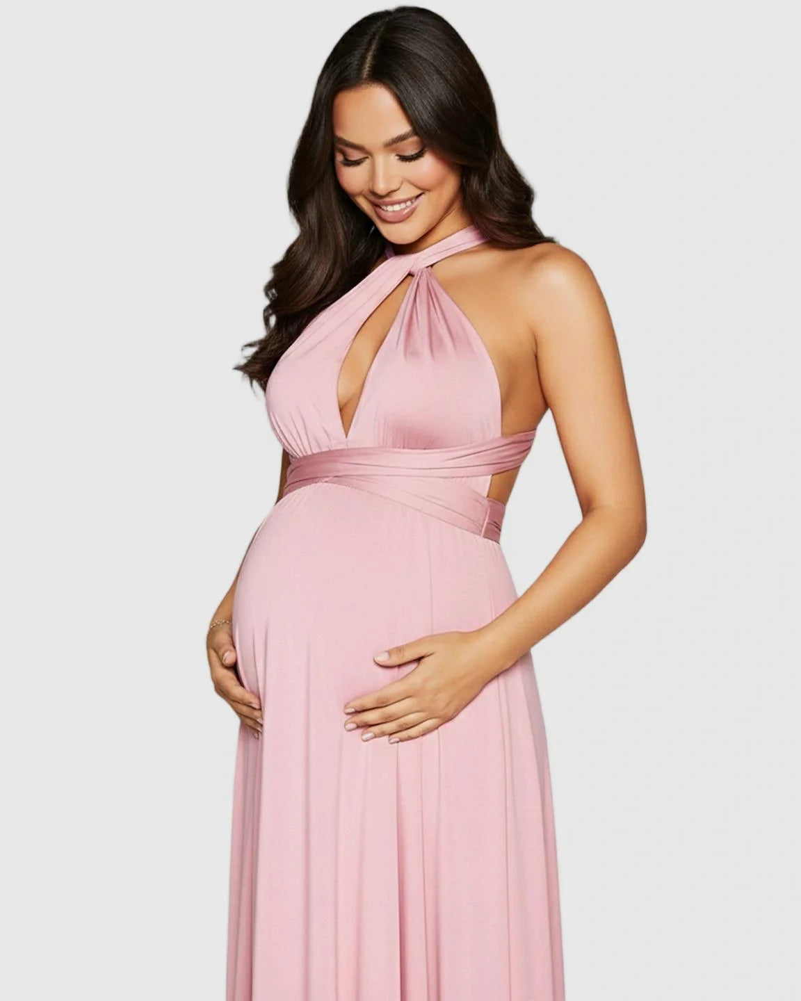 Smiling pregnant woman in a pink tie-waist flowy maternity maxi dress with a halter neckline.