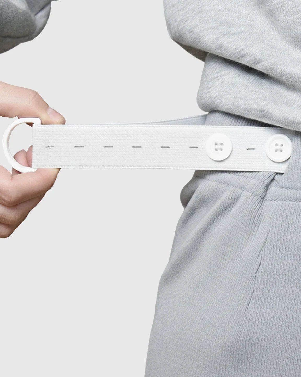 White elastic button extender for maternity pants, shown on light gray sweatpants.
