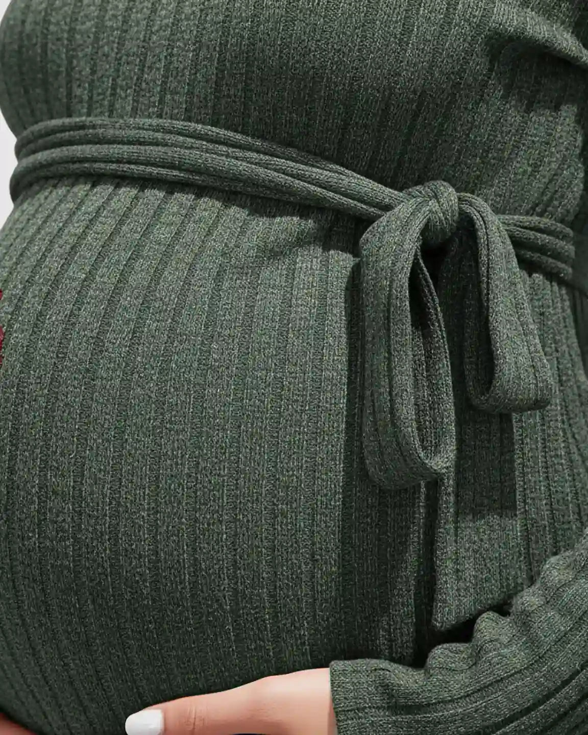 Close-up of a pregnant belly in a dark green ribbed tie-waist maternity sweater.
