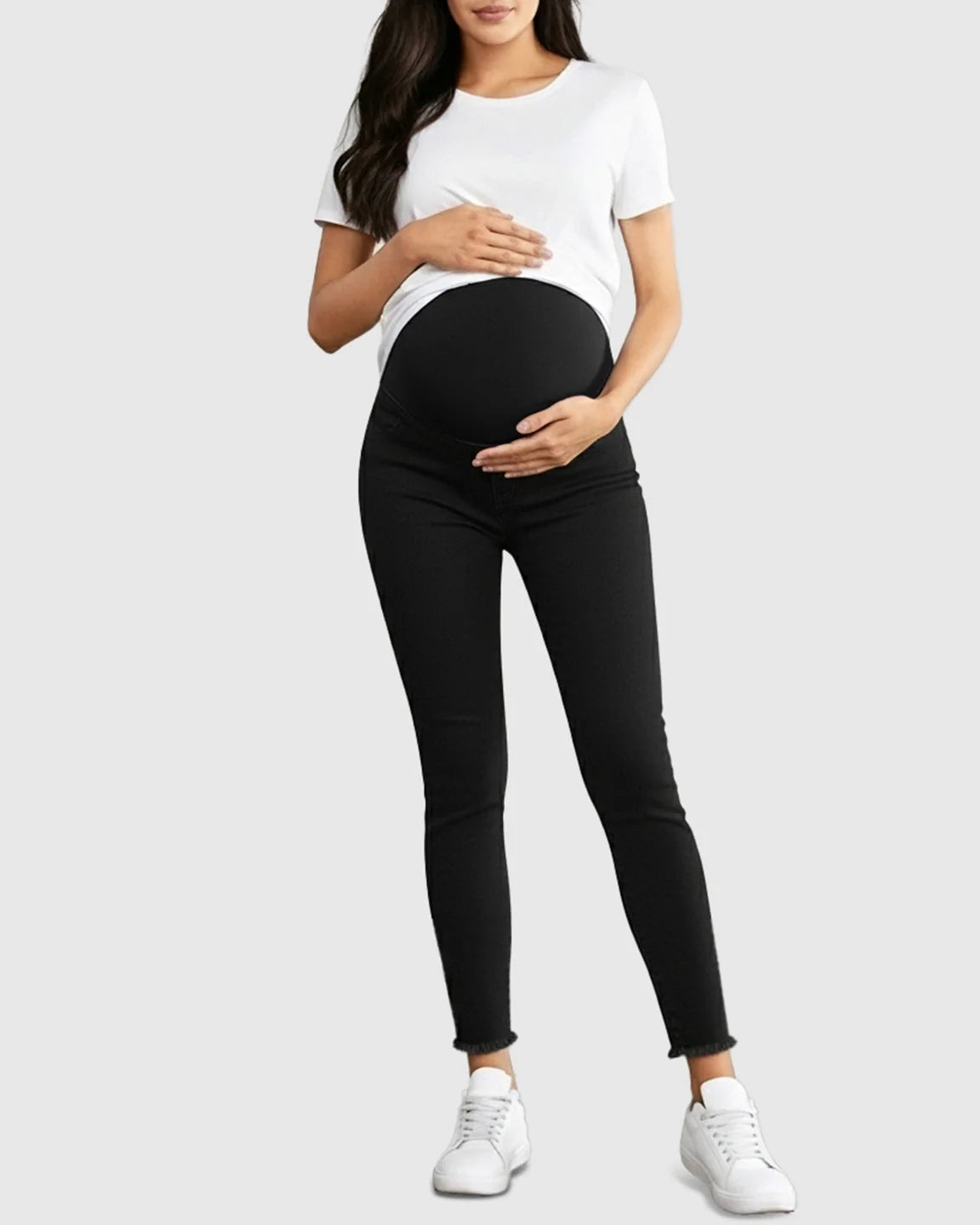 Woman wearing black stretch high-waist skinny maternity jeans with a supportive elastic belly band and raw hem.