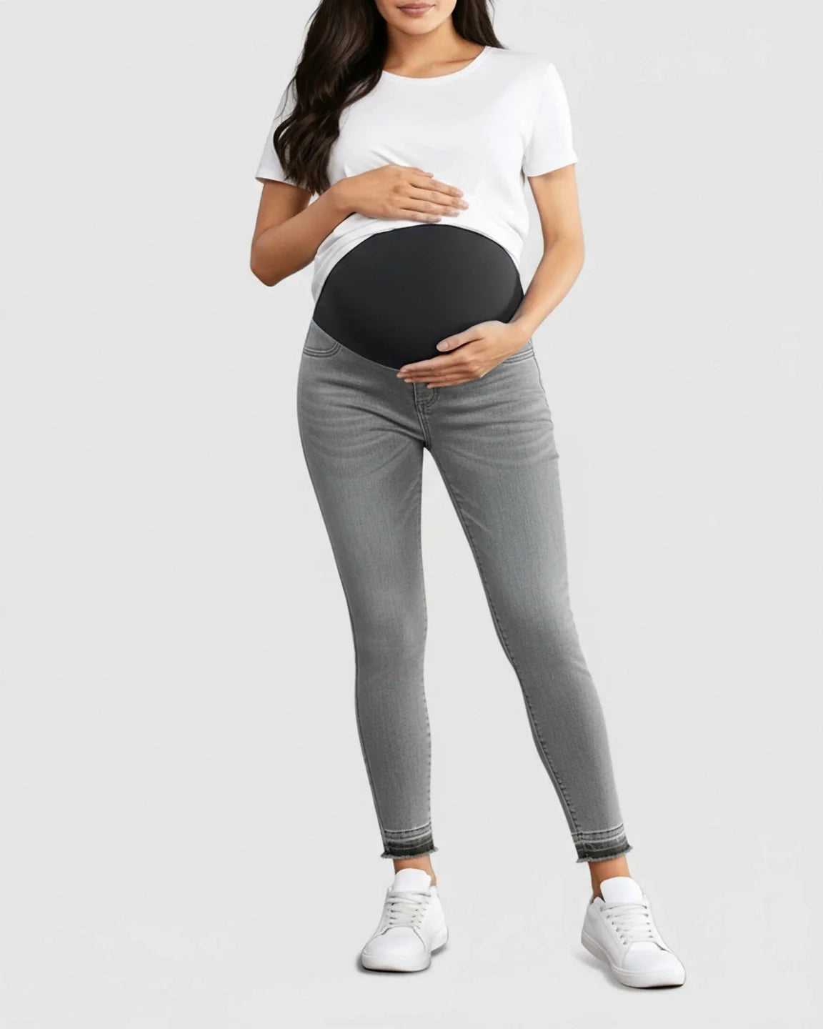 Woman wearing gray stretch high-waist skinny maternity jeans with a black elastic belly band and frayed hems.