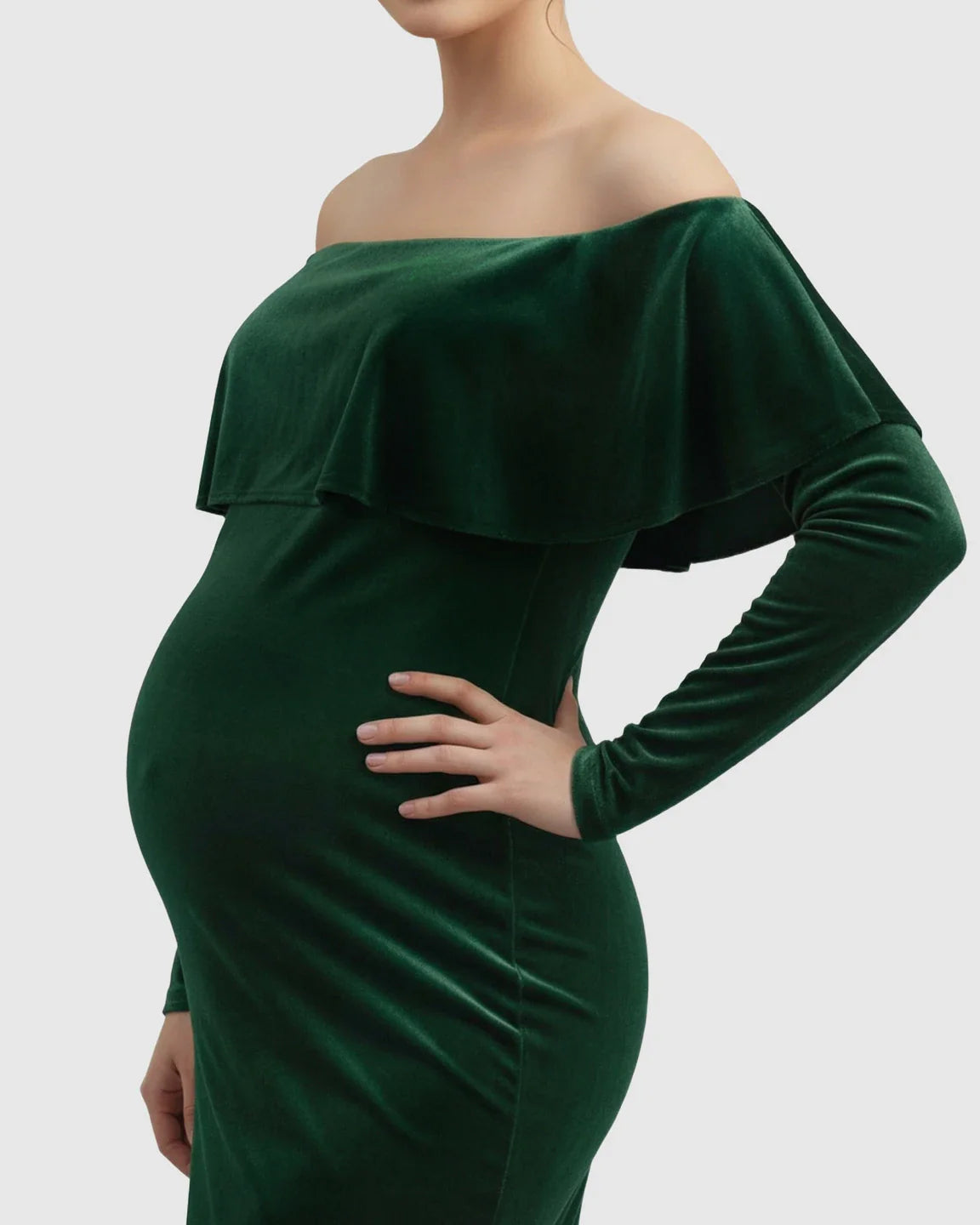 Emerald green velvet off-shoulder maternity gown with long sleeves, highlighting a pregnant belly.