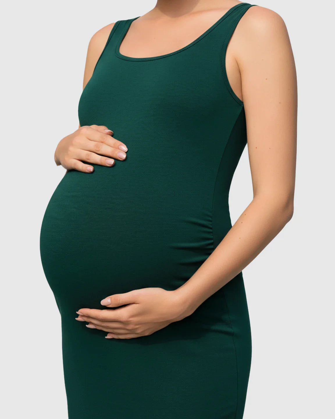 Pregnant woman in a dark green, side-ruched scoop neck bodycon maternity dress, cradling her bump.