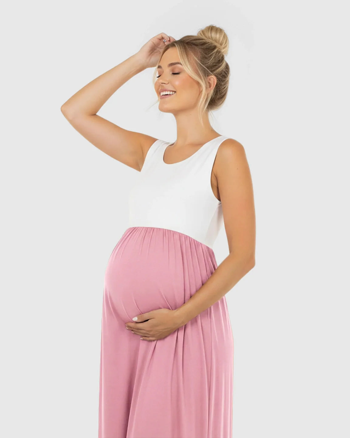 Smiling pregnant woman in a white and pink colorblock high-waisted maternity maxi dress, holding her bump.