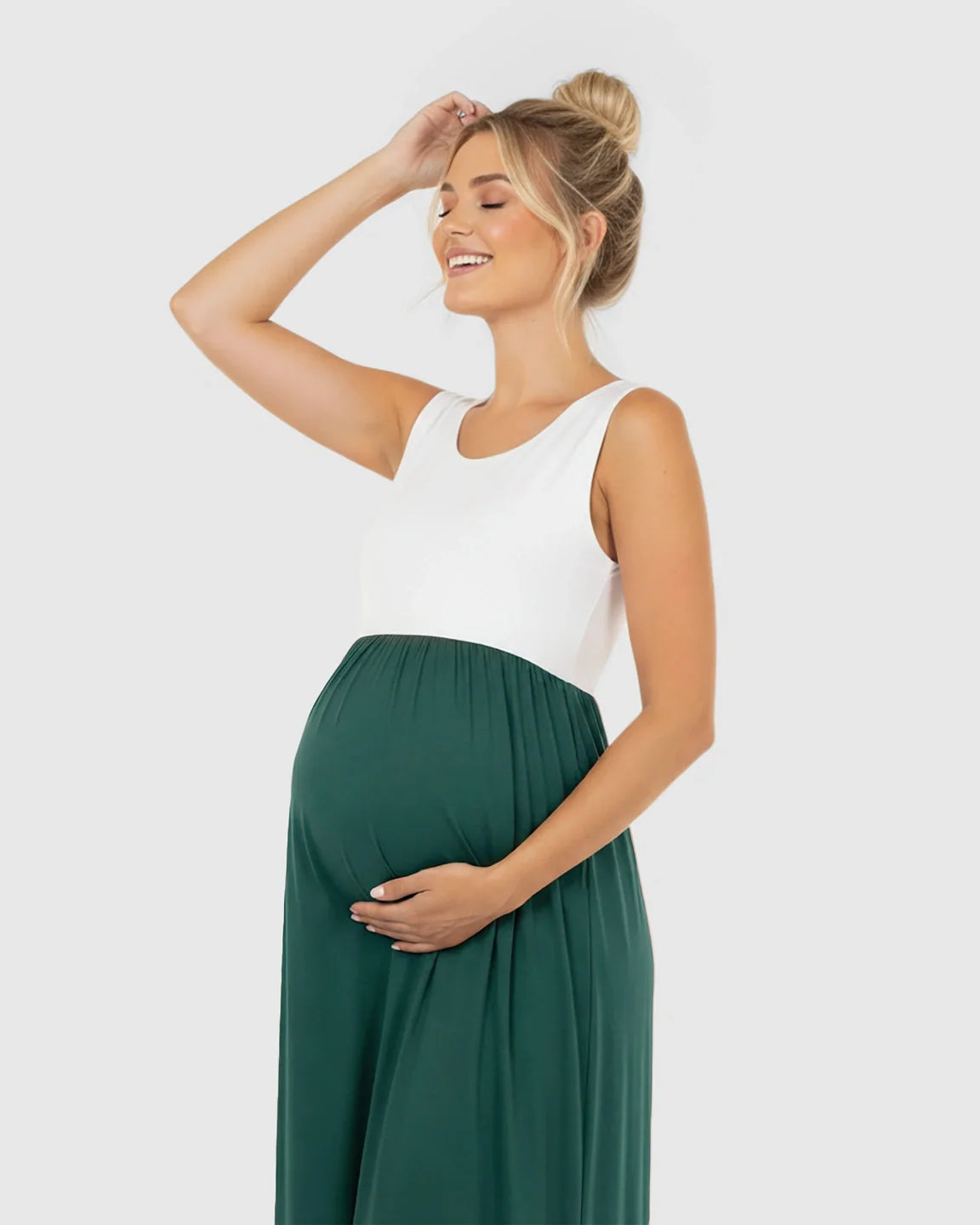 Smiling pregnant woman in a sleeveless white and dark green colorblock high-waisted maternity maxi dress.