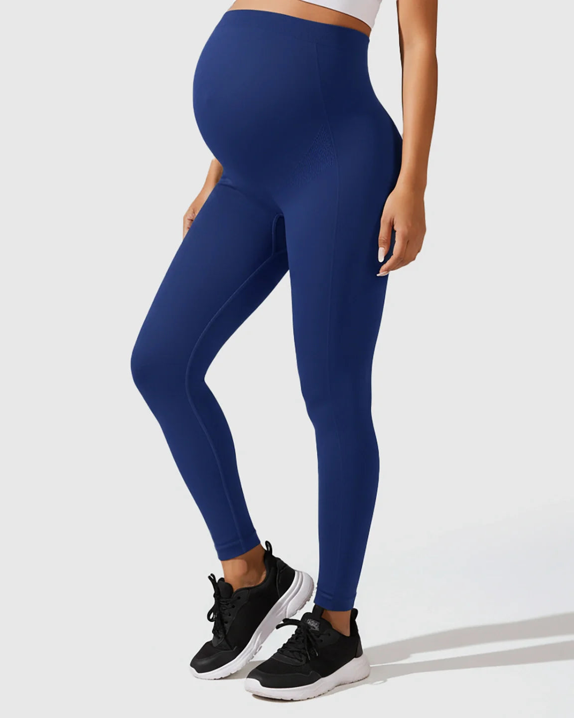 Pregnant woman wearing seamless navy blue M-shape maternity leggings with full-belly support.