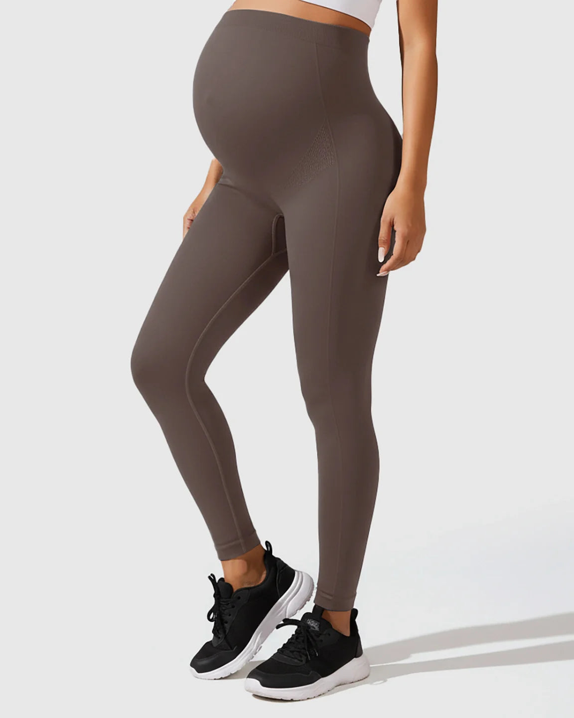 Pregnant woman wearing seamless, high-waisted, full-belly support, M-shape maternity leggings in a dark brown color.