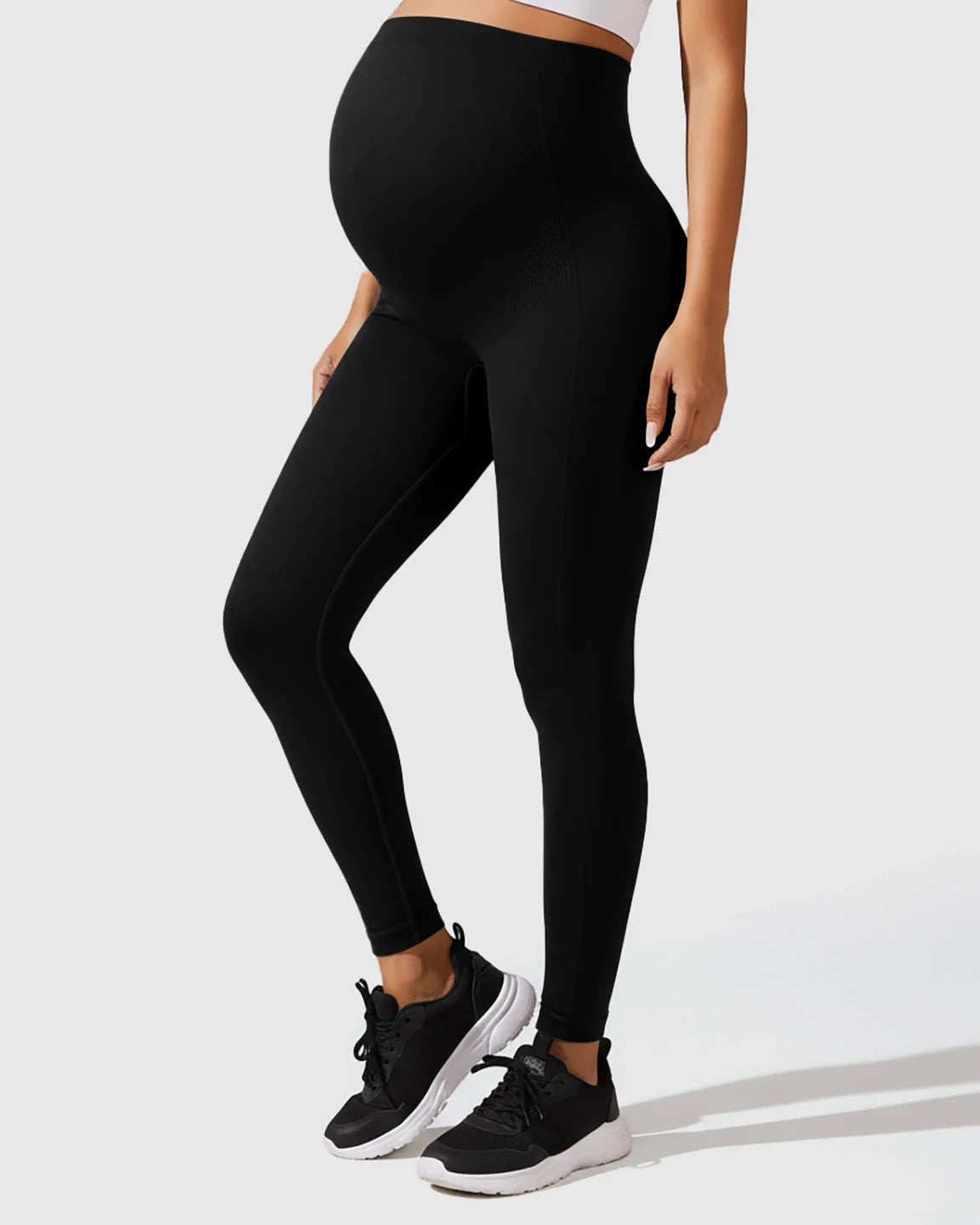 Pregnant model wearing black seamless M-shape maternity leggings with full-belly support and black sneakers.