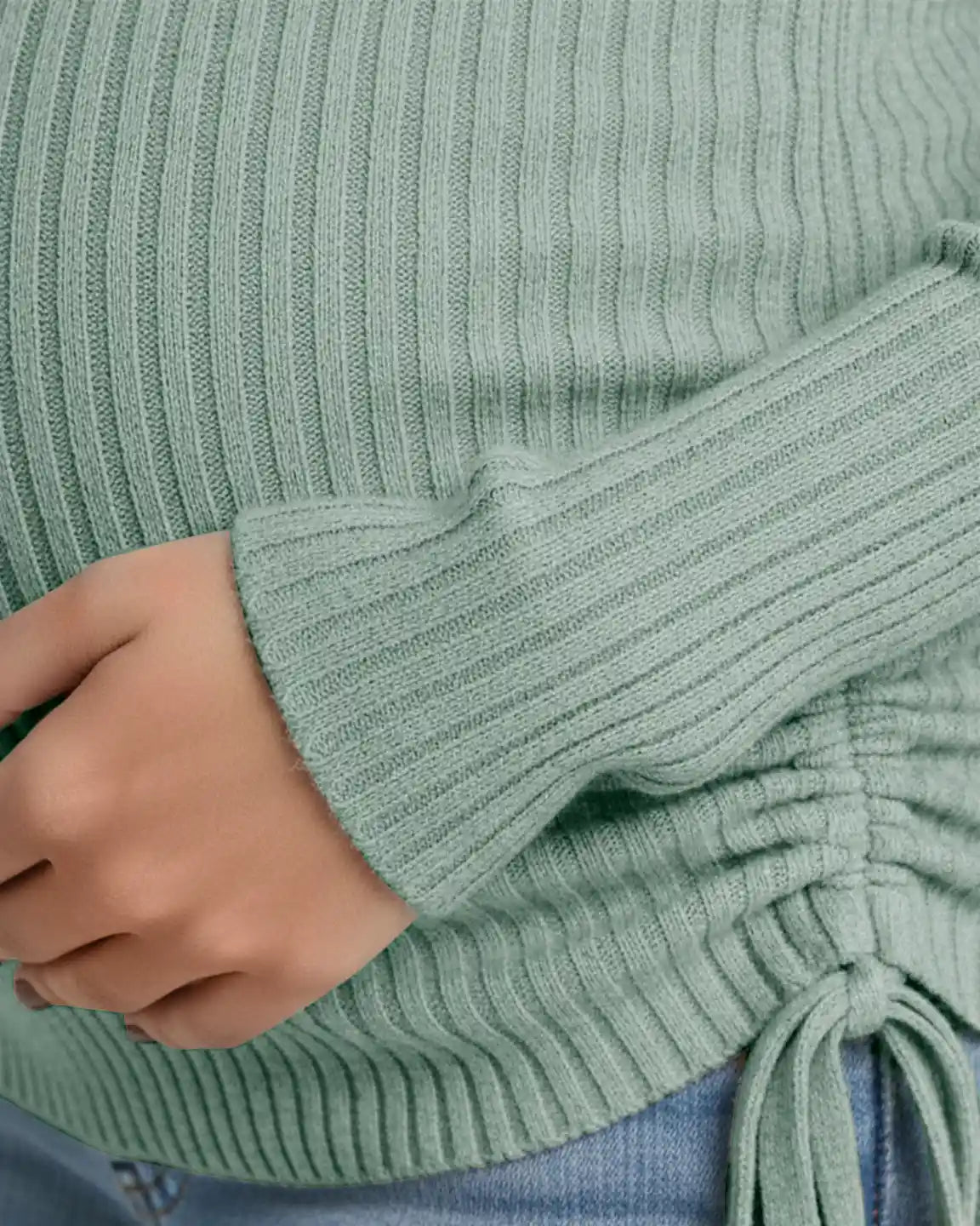 Close-up of a pregnant woman wearing a sage green ribbed maternity top with adjustable side drawstrings.