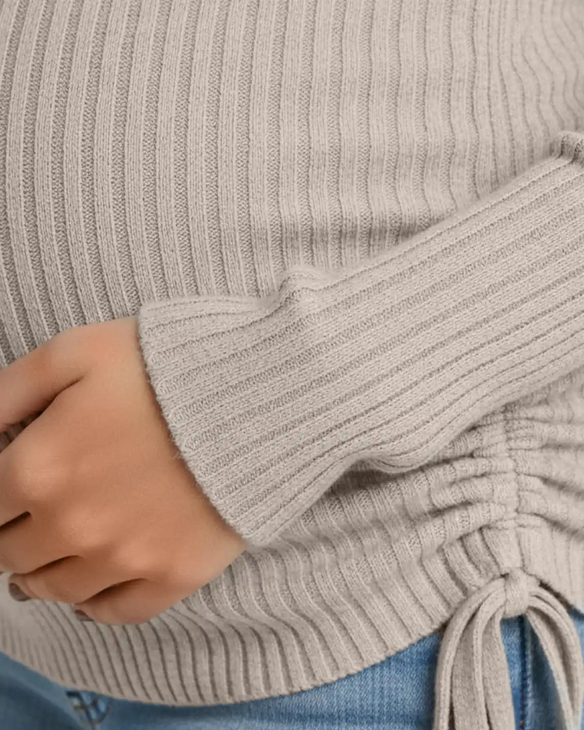 Close-up of a pregnant woman wearing a light beige ribbed maternity top with adjustable side drawstrings.