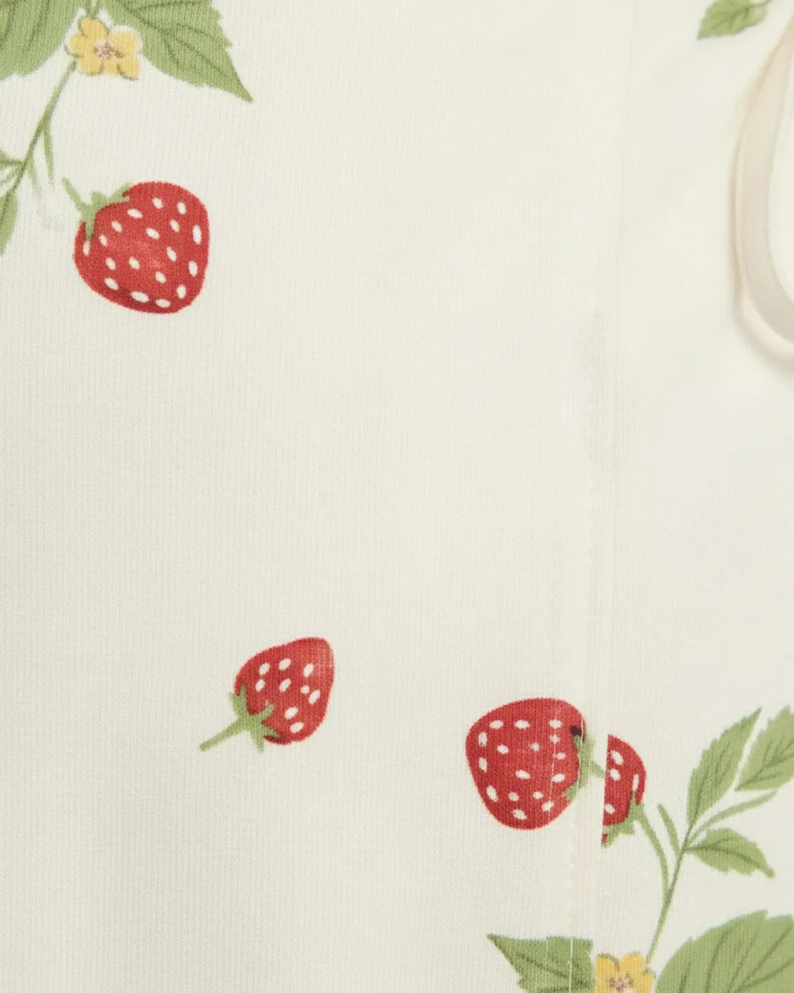 Close-up of white cotton gauze fabric with red strawberry and green leaf print, featuring a tie detail.