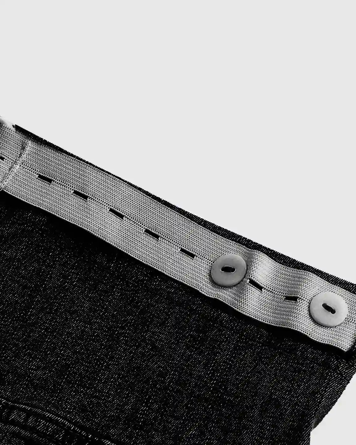 Close-up of black stretch denim maternity jeans with adjustable grey elastic waistband and buttons.
