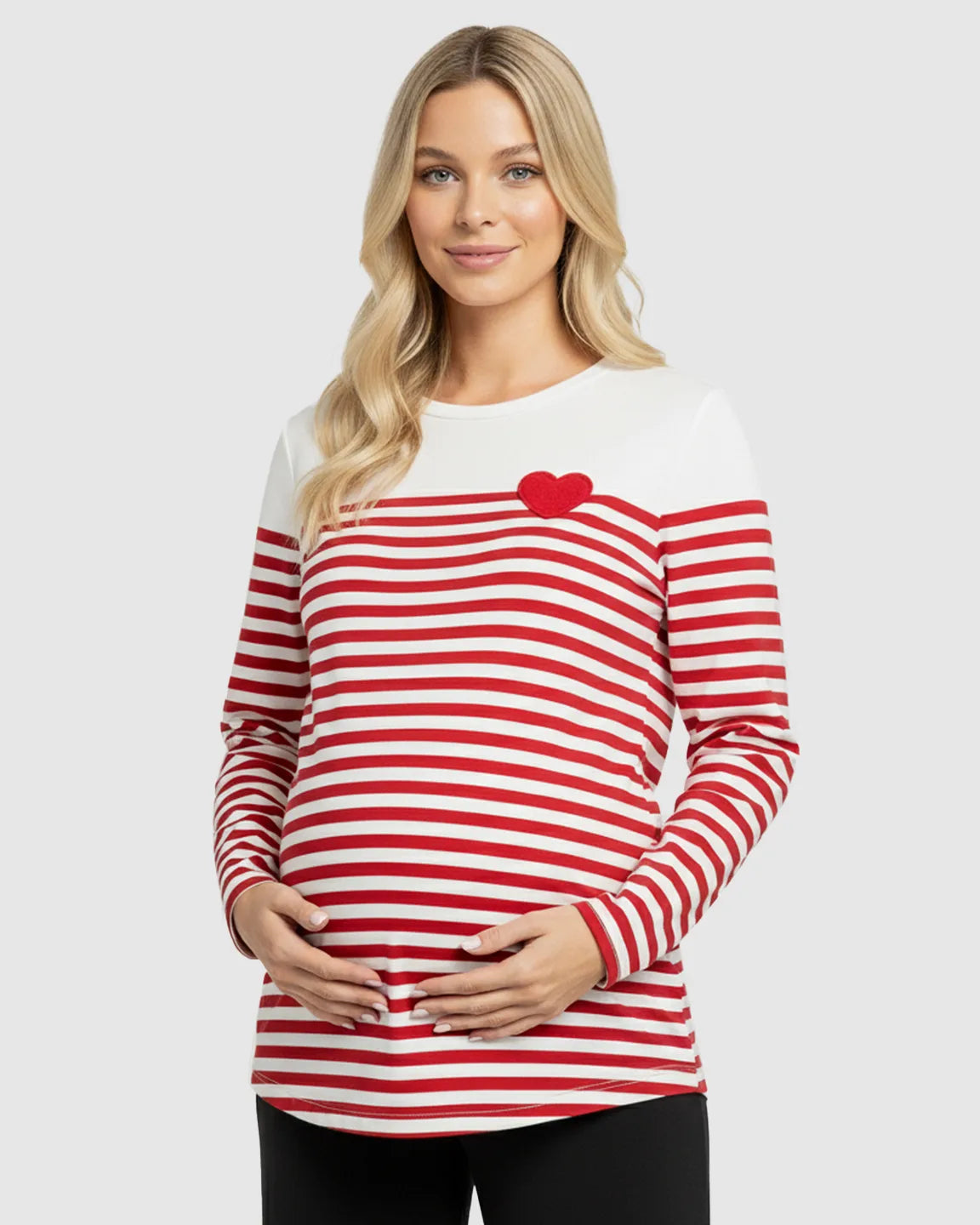 Blonde pregnant woman wearing a red and white striped long-sleeve maternity top with a red heart.