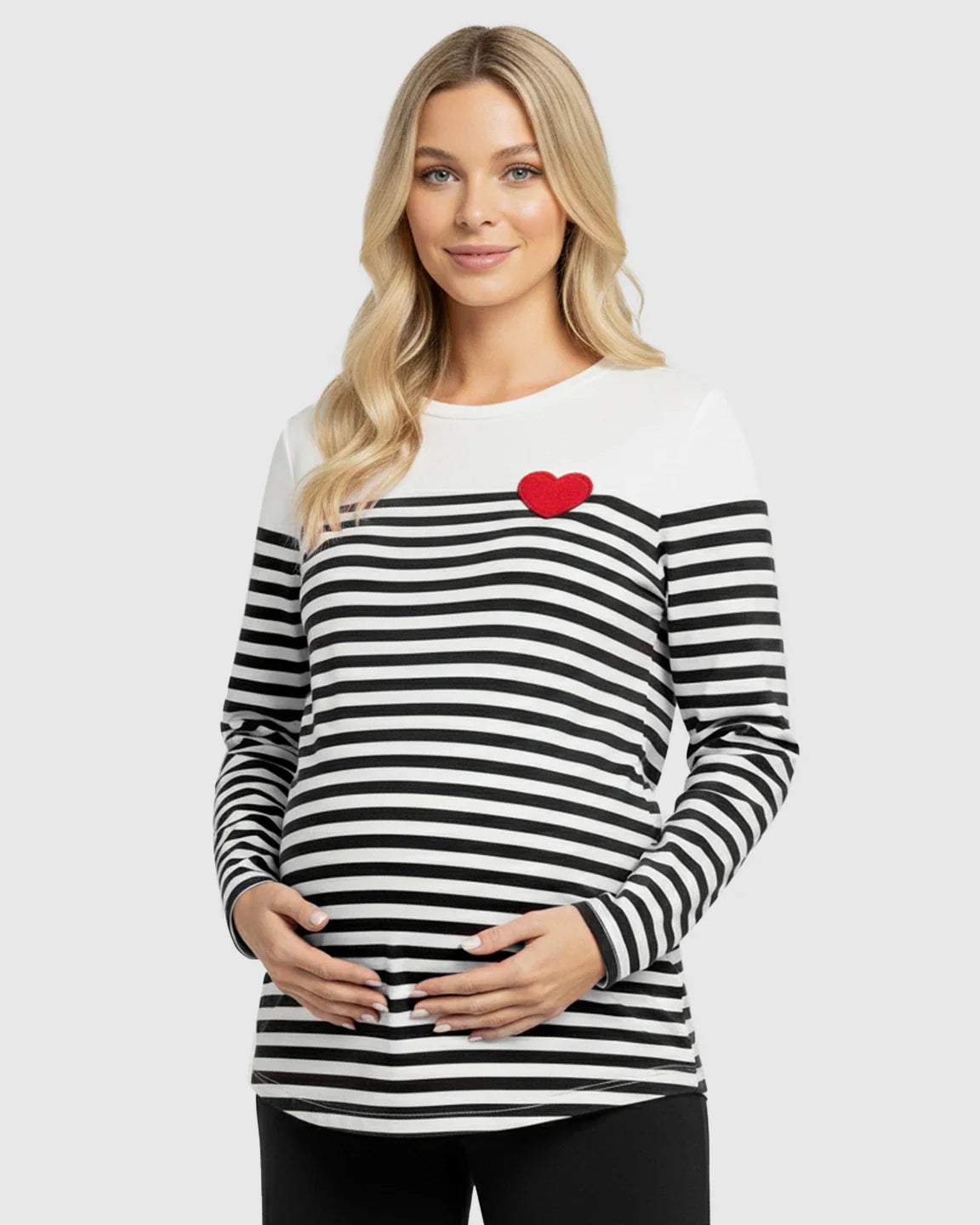 Blonde pregnant woman wearing a black and white striped long-sleeve maternity top with a red heart.