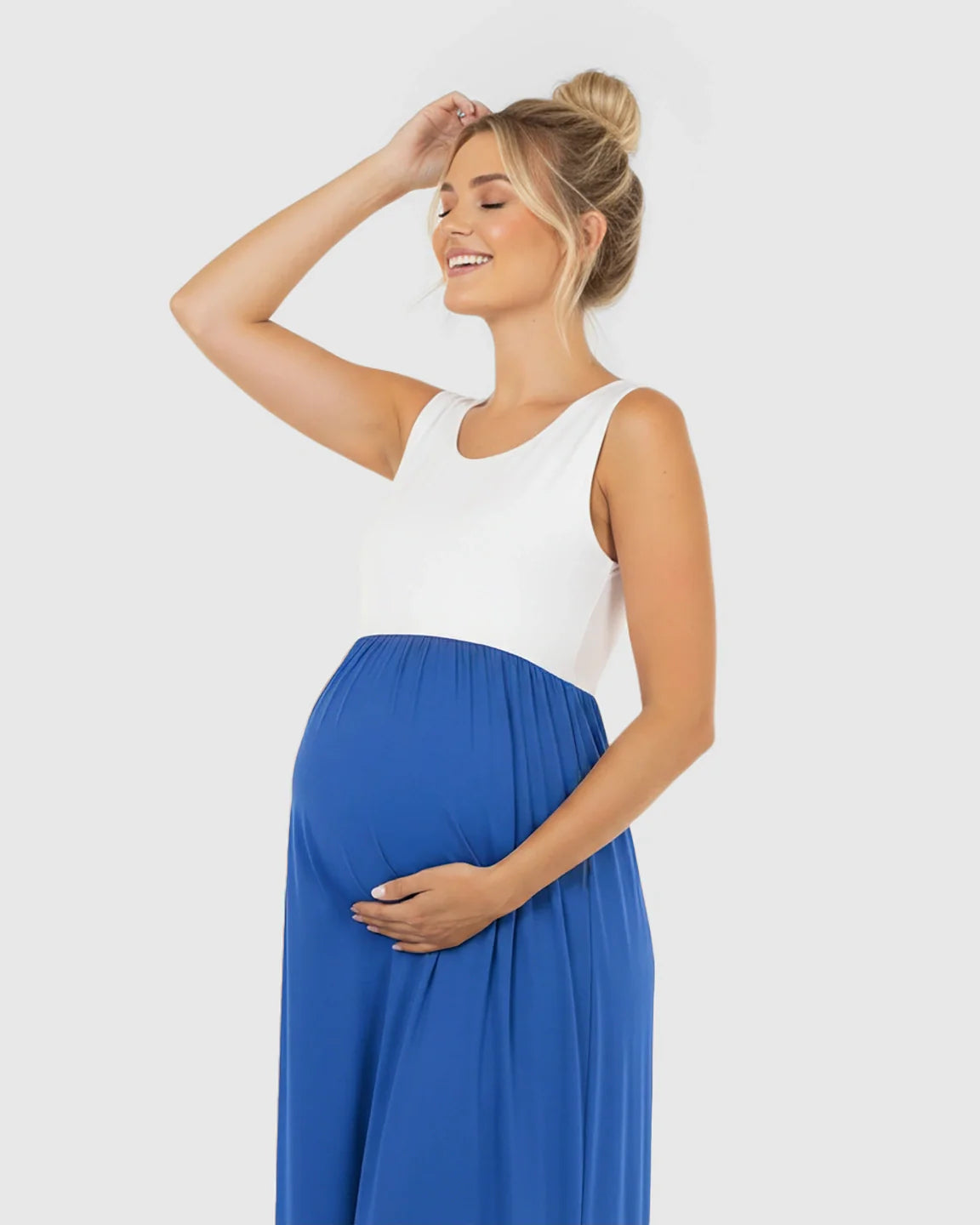 Smiling pregnant woman in a white and royal blue colorblock high-waisted maternity maxi dress.