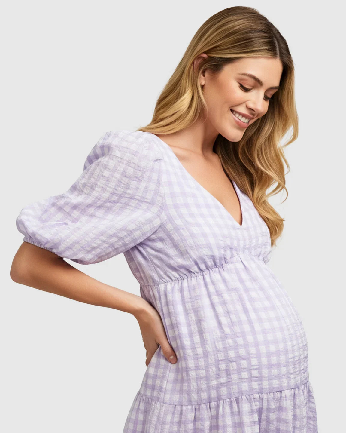 Smiling pregnant woman in a lavender and white checkered maternity maxi dress with puffed sleeves.