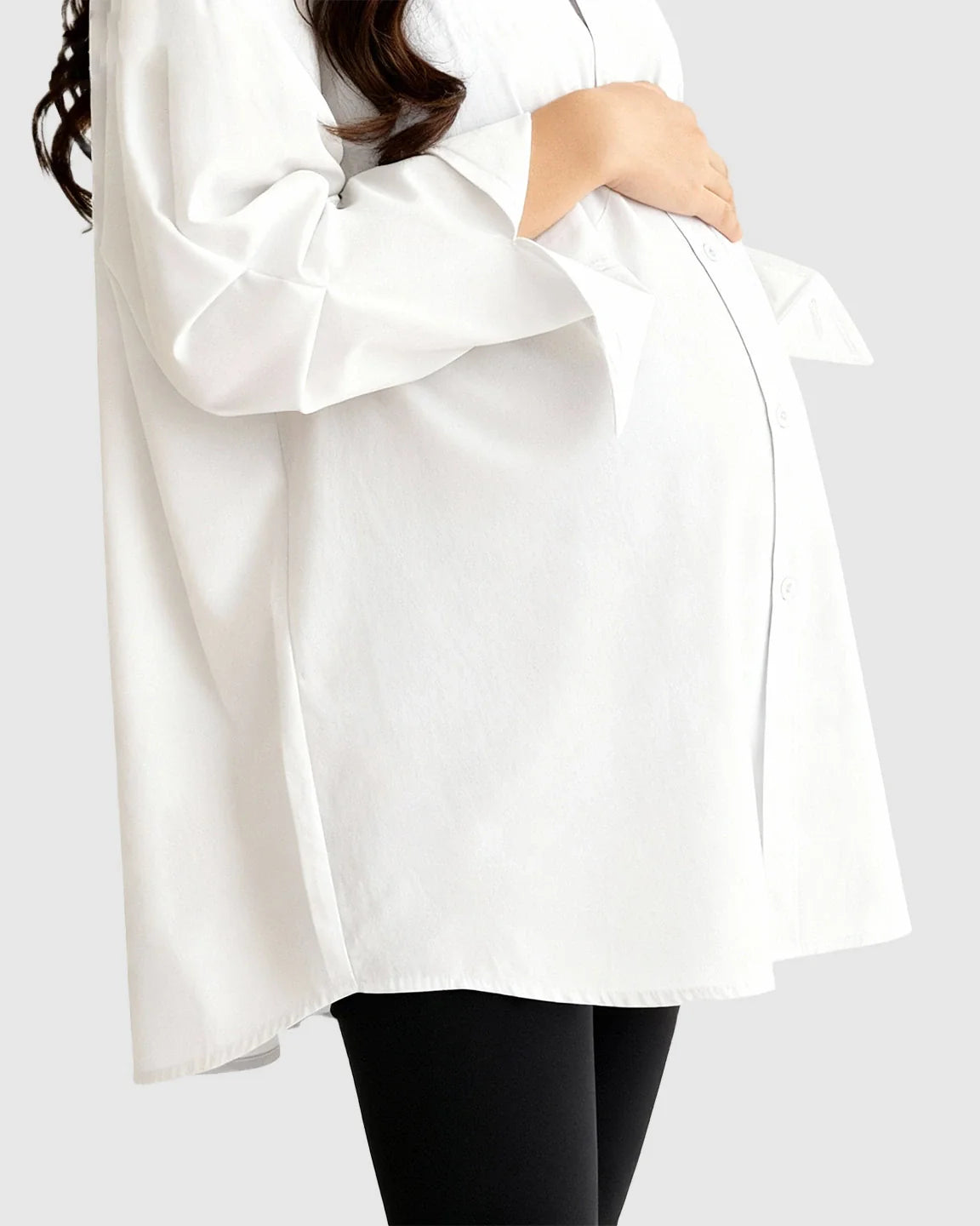 Pregnant woman in a white cotton lapel-collar button-front maternity tunic over black leggings.