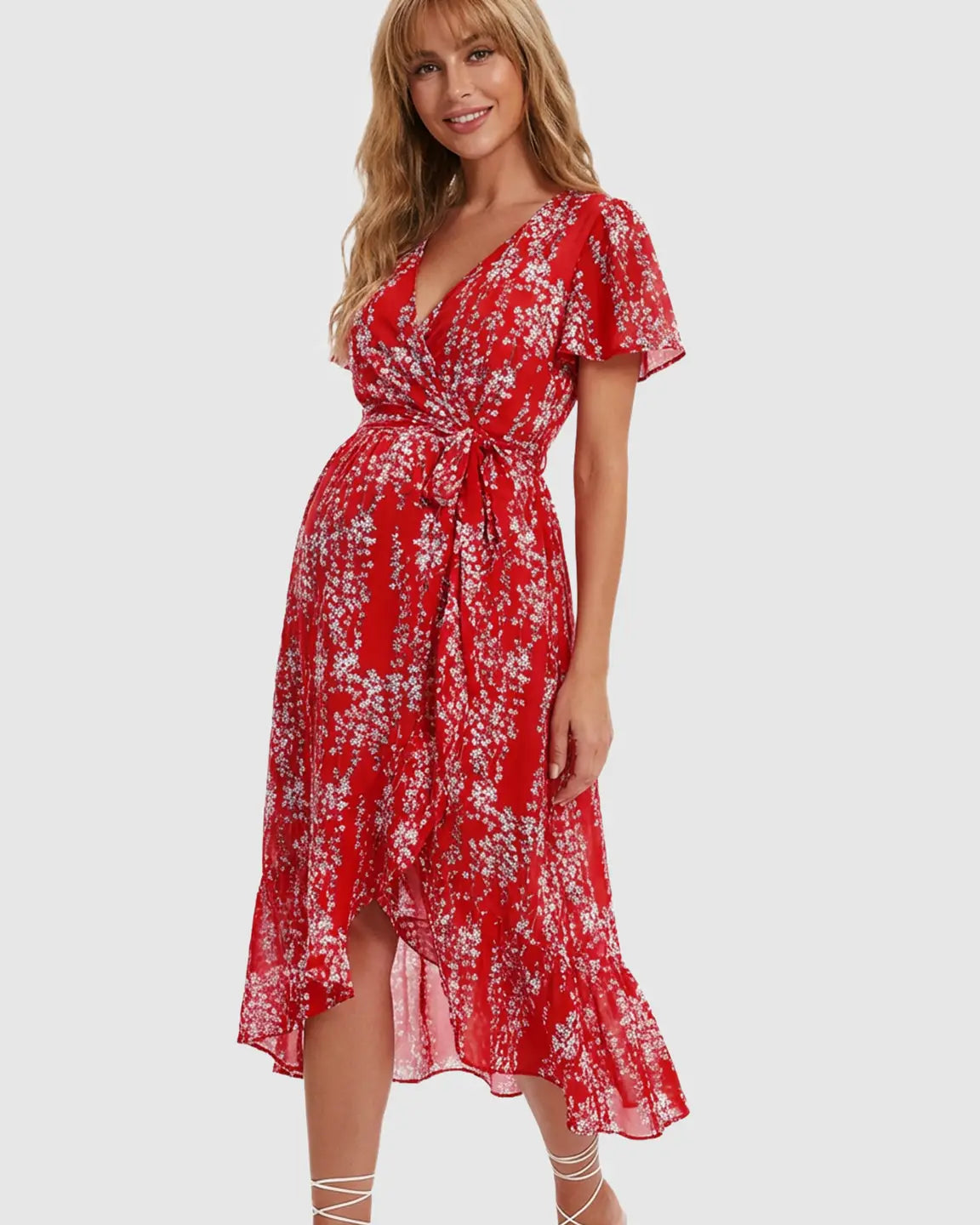 Smiling pregnant woman in a red floral V-neck maternity midi dress with ruffled hem and tie waist.