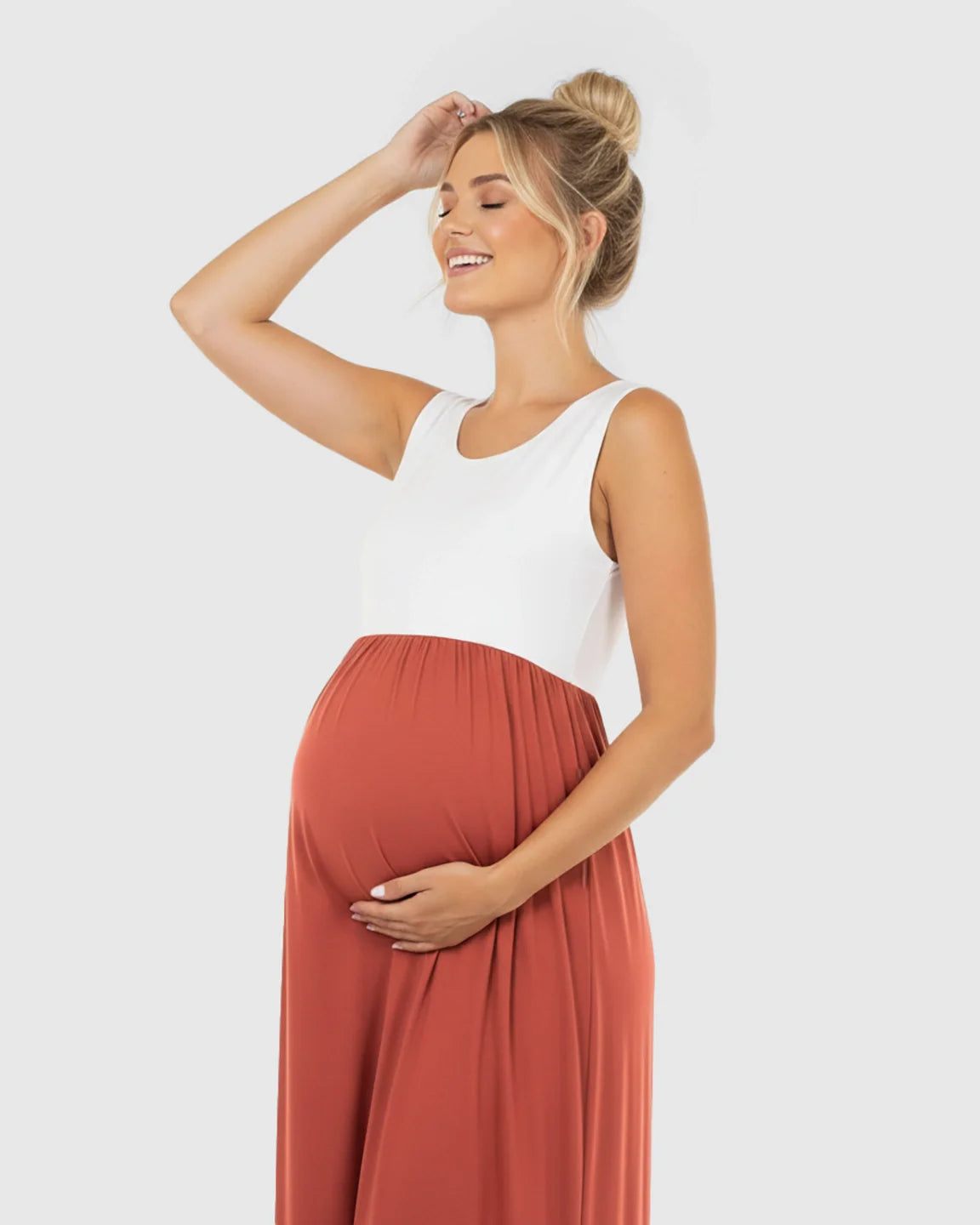 Smiling pregnant woman in a white and rust colorblock high-waisted maternity maxi dress, holding her bump.
