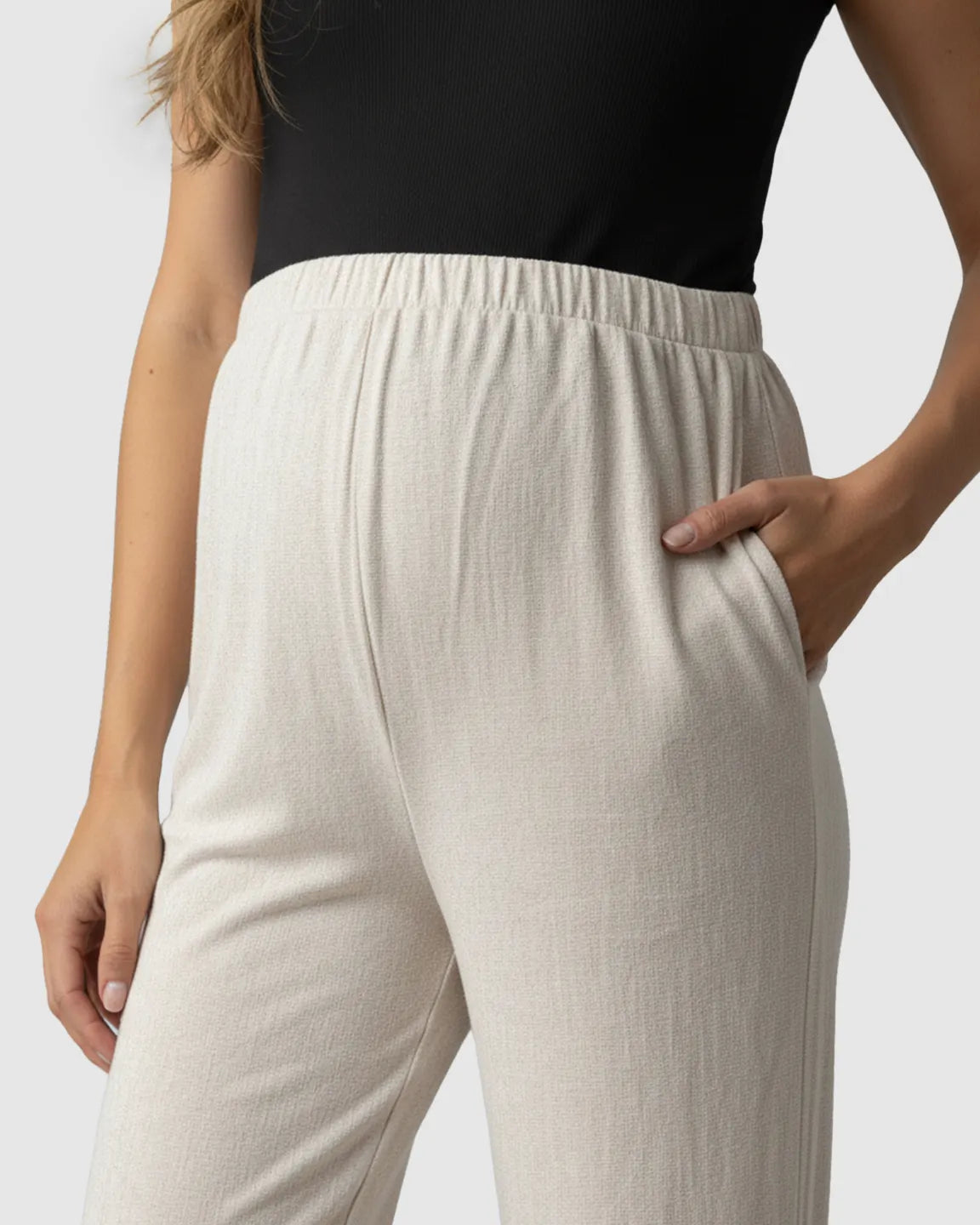 Close-up of Bump Society's beige elastic waist wide-leg maternity pants with a hand in the pocket.