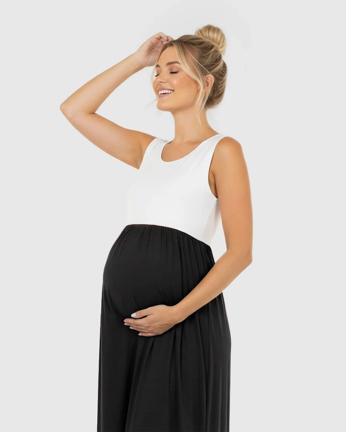 Smiling pregnant woman in a sleeveless white and black colorblock high-waisted maternity maxi dress.