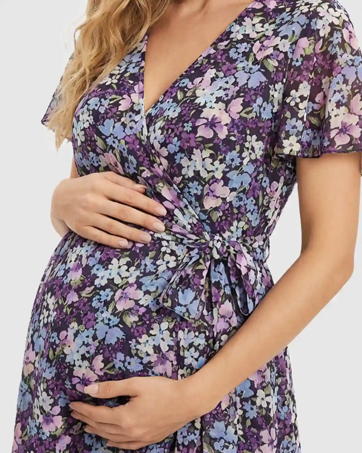 Maternity midi dress in purple floral print with V-neck, flutter sleeves, and tie-waist over a baby bump.