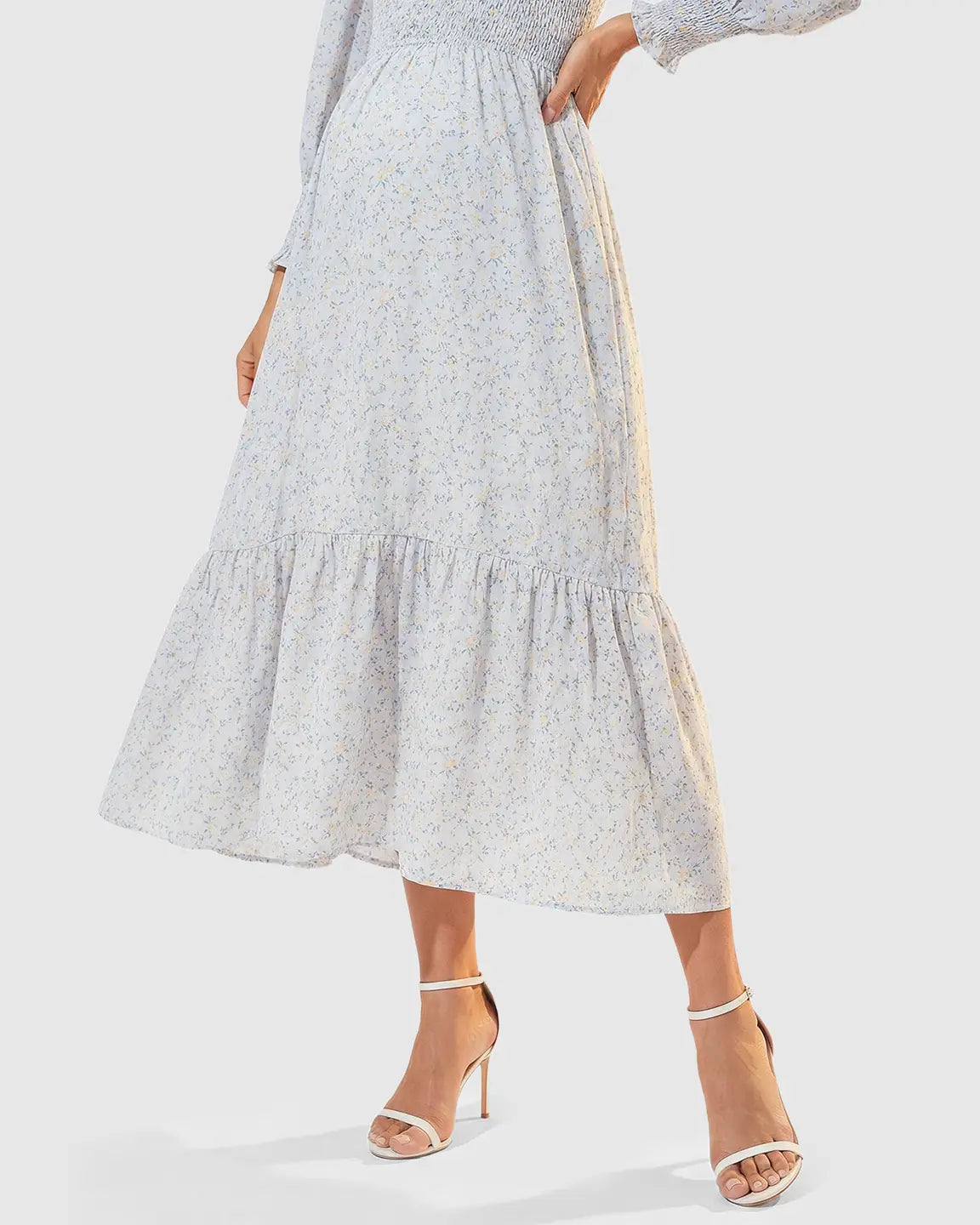 Light blue smocked floral long sleeve maternity midi dress with ruffled hem, worn with white heels.