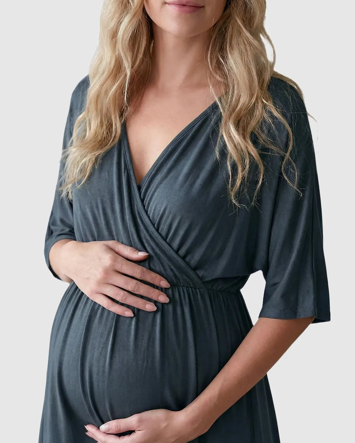 Pregnant woman in a dark gray cross-front maternity midi dress with 3/4 sleeves, hands on her bump.