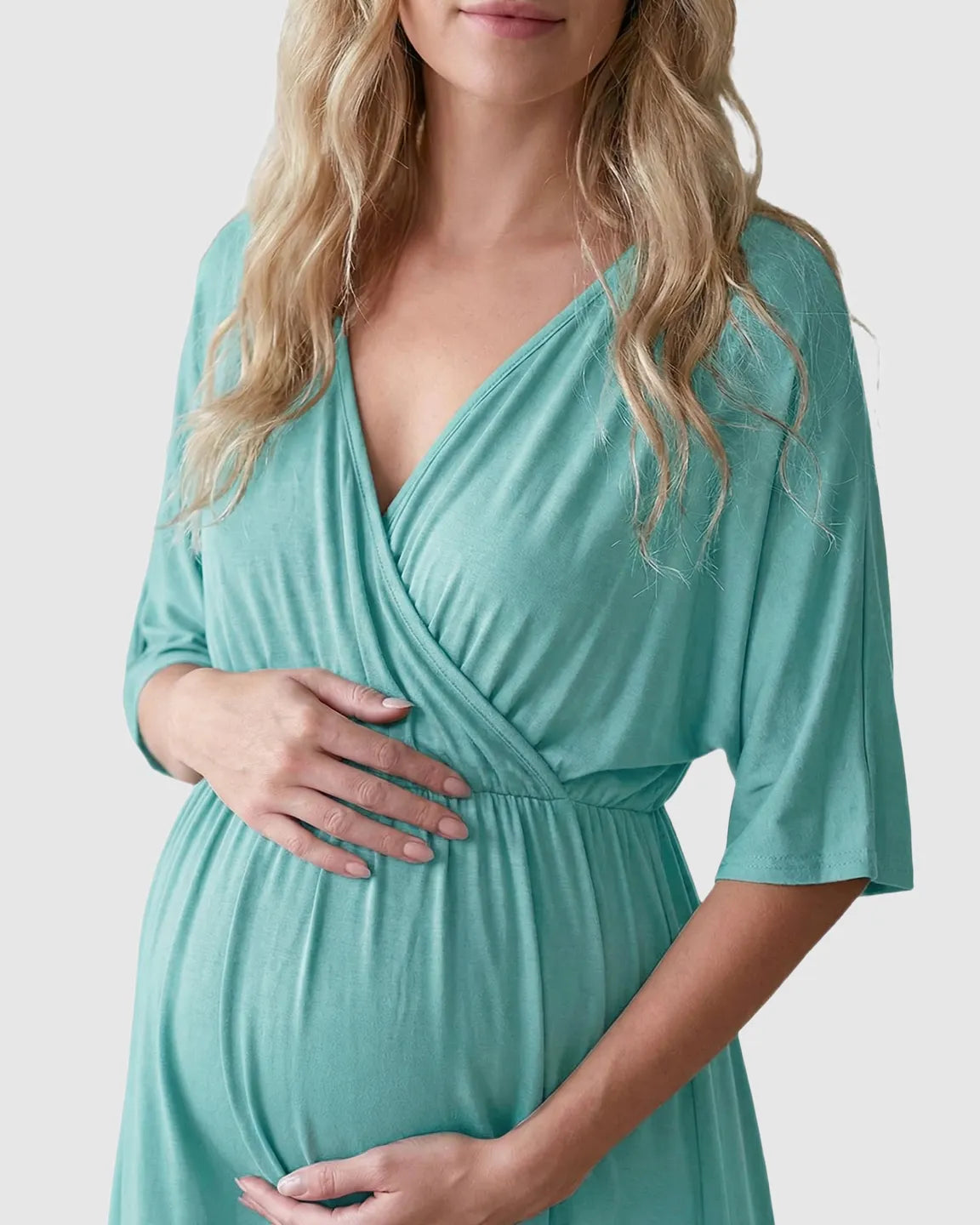 Pregnant woman in a mint green cross-front maternity midi dress with 3/4 sleeves, holding her bump.