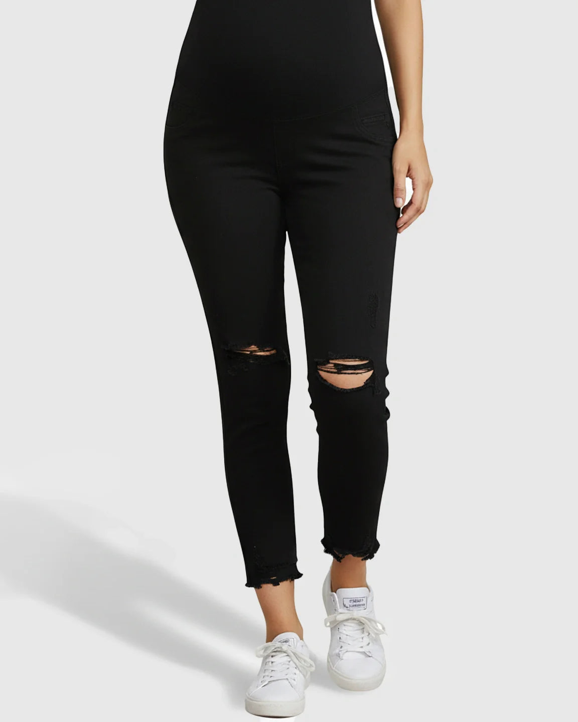 Black maternity skinny jeans with over-belly support panel, distressed knees, and ankle-fray hem.