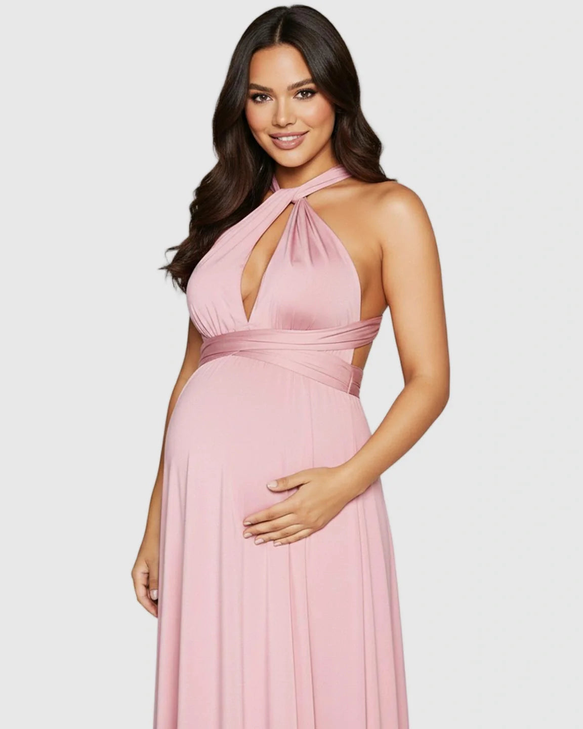 Smiling pregnant woman in a pink tie-waist flowy maternity maxi dress with a halter neckline.