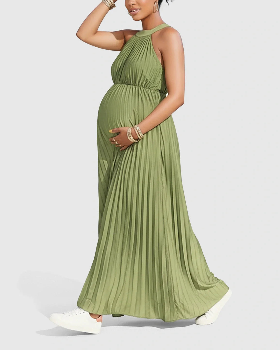 Pregnant woman in a flowing olive green halter neck pleated maternity maxi dress, faux silk, with white sneakers.