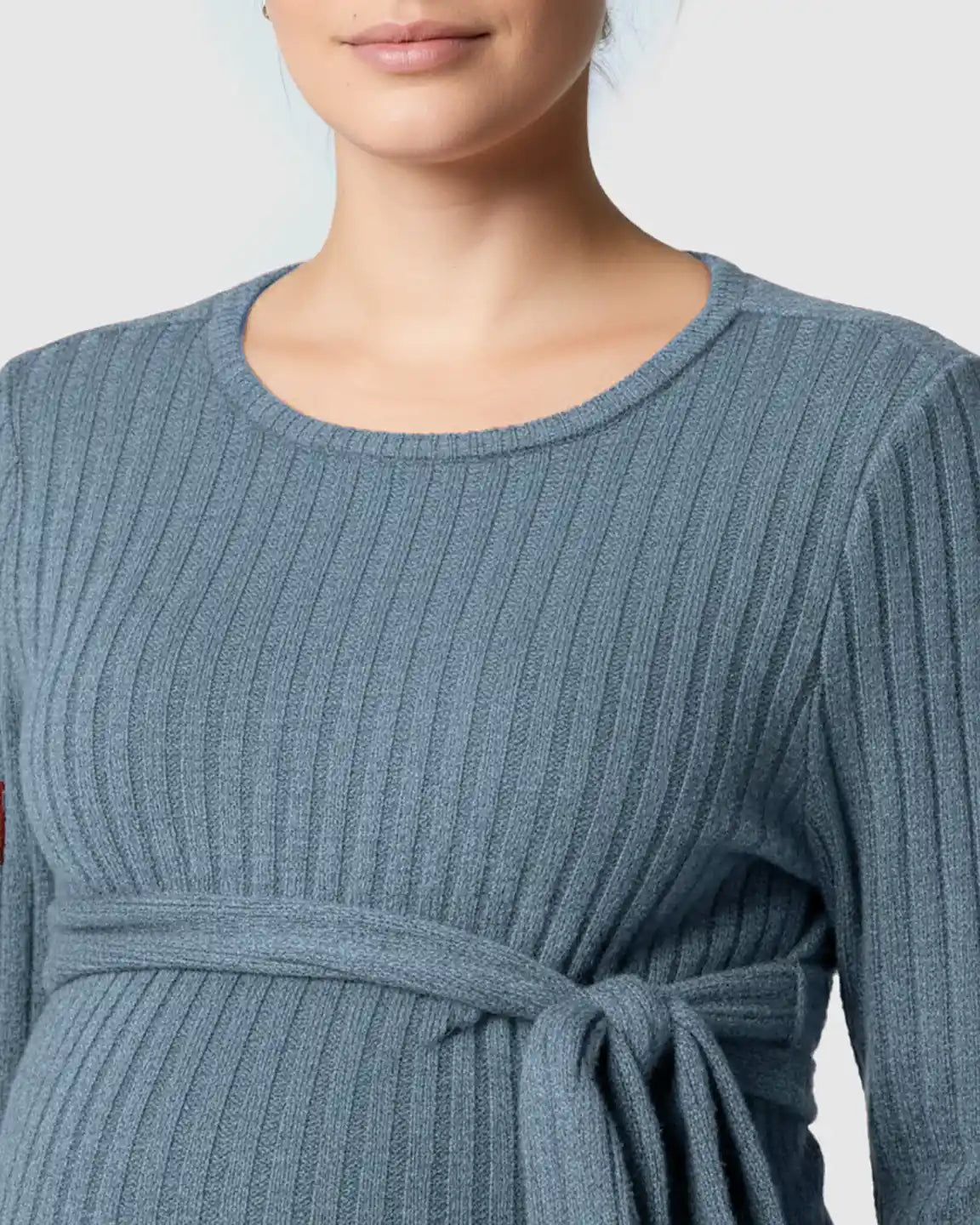 Close-up of a pregnant woman wearing a blue ribbed tie-waist long sleeve maternity sweater.