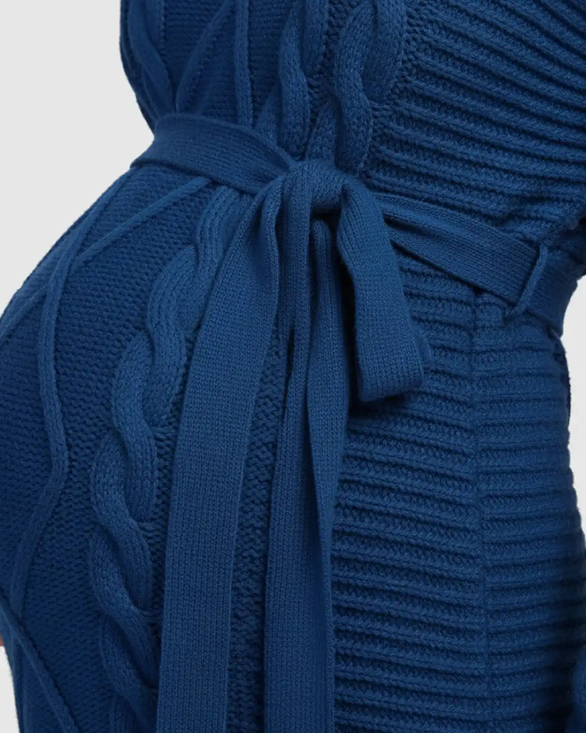 Close-up of a blue knitted maternity midi dress with a tie-waist, high-neck, and cable knit details.