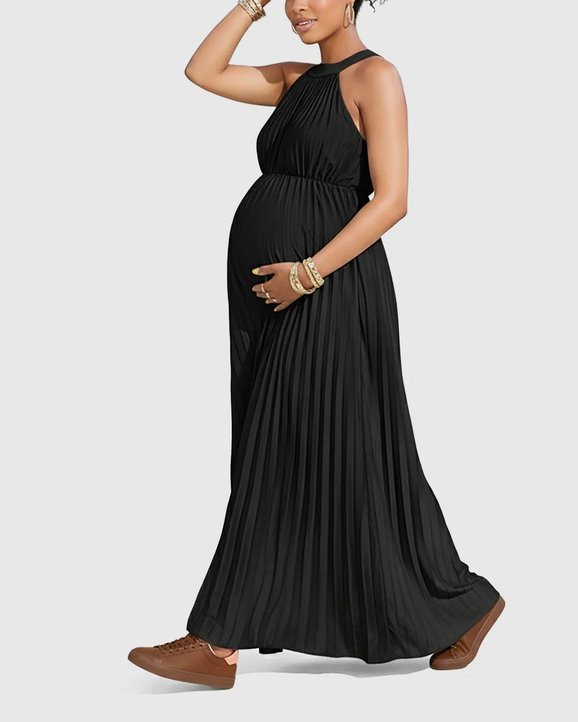 Pregnant woman in a black halter neck pleated faux silk maternity maxi dress, holding her baby bump.