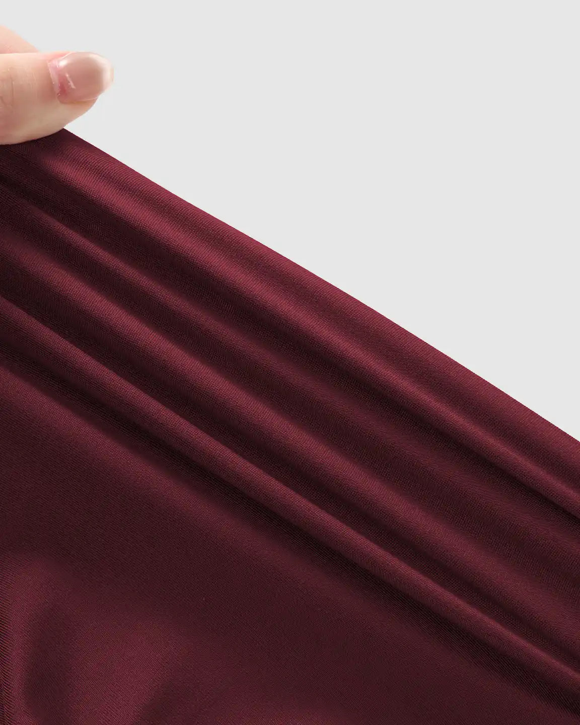 Hand stretching the soft, breathable burgundy fabric of supportive slim-fitting maternity joggers.