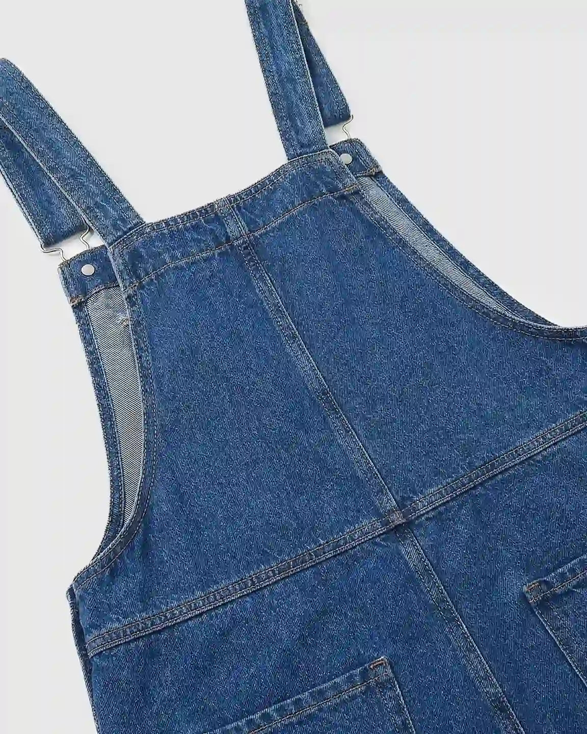 Close-up of a blue denim maternity jumpsuit with adjustable straps and visible stitching.